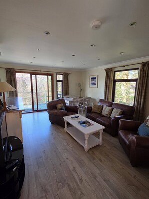 A spacious living room with a large sofa set, a coffee table, and a dining area with a table and chairs. - Beautiful 4 star 2 bedroom chalet with stunning loch and mountain views (Crianlarich)