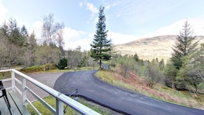 A wooden deck with chairs overlooking a winding road and a mountainous landscape. - Beautiful 4 star 2 bedroom chalet with stunning loch and mountain views (Crianlarich)
