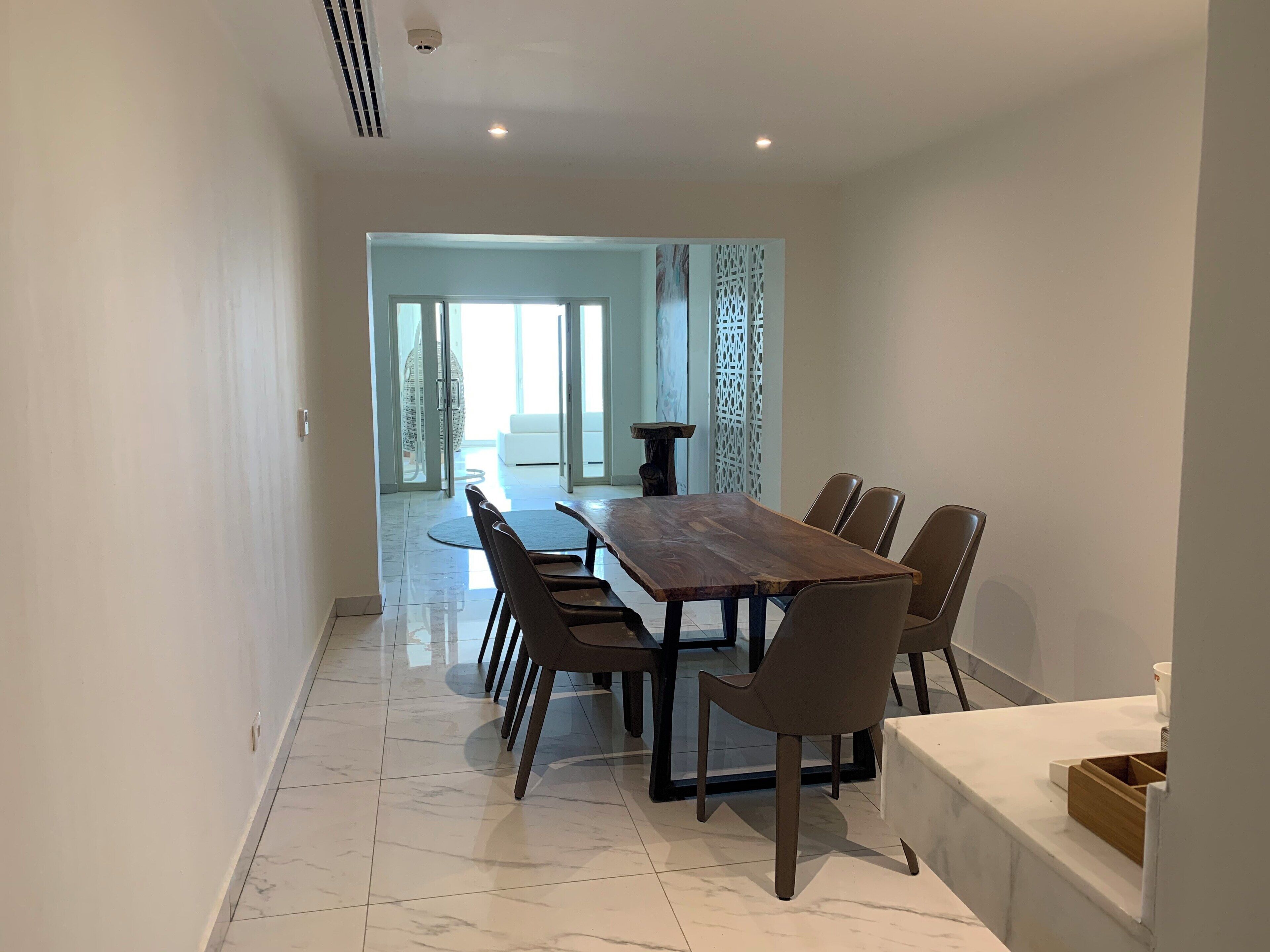 A modern dining area with a rectangular wooden table and six chairs, a white countertop, and a marble floor.