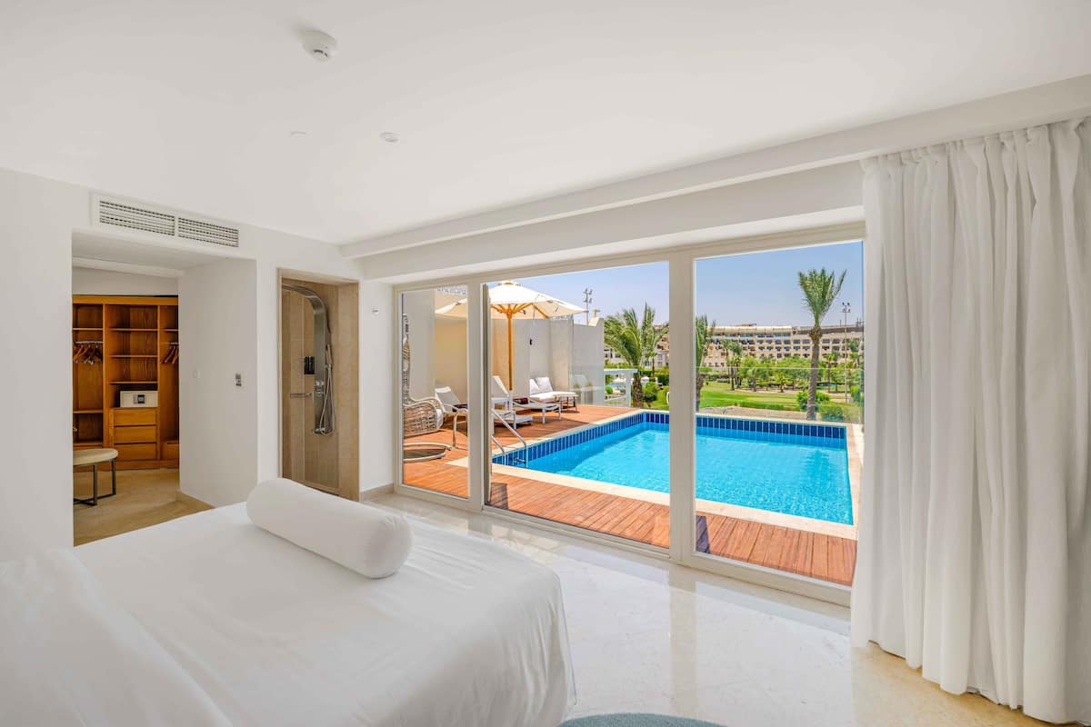A hotel room with a large bed, a walk-in closet, a bathroom with a shower, and a view of an outdoor swimming pool.