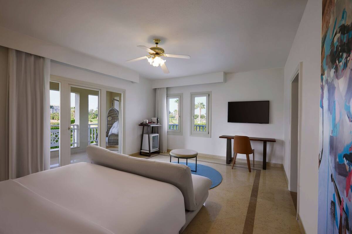 A hotel room with a large bed, a desk, a chair, a television, and a balcony with a view.