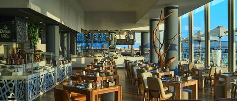 A spacious restaurant with high ceilings and large windows offering views of the city.