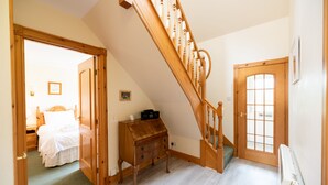 A bedroom with a wooden bed, a nightstand, and a dresser. There is a staircase leading to another room. - 4 star, 4 bedroom, 3 bathroom Scottish cottage with sensational loch and mountain views (Crianlarich)