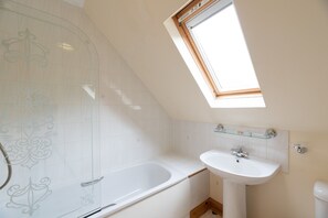 A bathroom with a bathtub, a glass shower enclosure, a sink, and a skylight.
