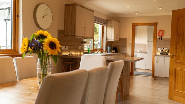 A modern kitchen with a dining area, wooden cabinets, and a clock on the wall. - 4 star, 4 bedroom, 3 bathroom Scottish cottage with sensational loch and mountain views (Crianlarich)