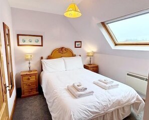 Une chambre à coucher avec un lit, deux tables de chevet, une fenêtre et un luminaire au plafond.
