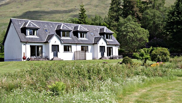 A large, white, two-story house with a sloped roof, multiple windows, and a front porch. - 4 star, 4 bedroom, 3 bathroom Scottish cottage with sensational loch and mountain views (Crianlarich)