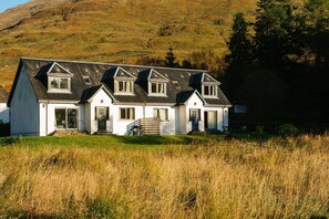 A two-story house with a steeply pitched roof, multiple windows, and a front porch. - 4 star, 4 bedroom, 3 bathroom Scottish cottage with sensational loch and mountain views (Crianlarich)