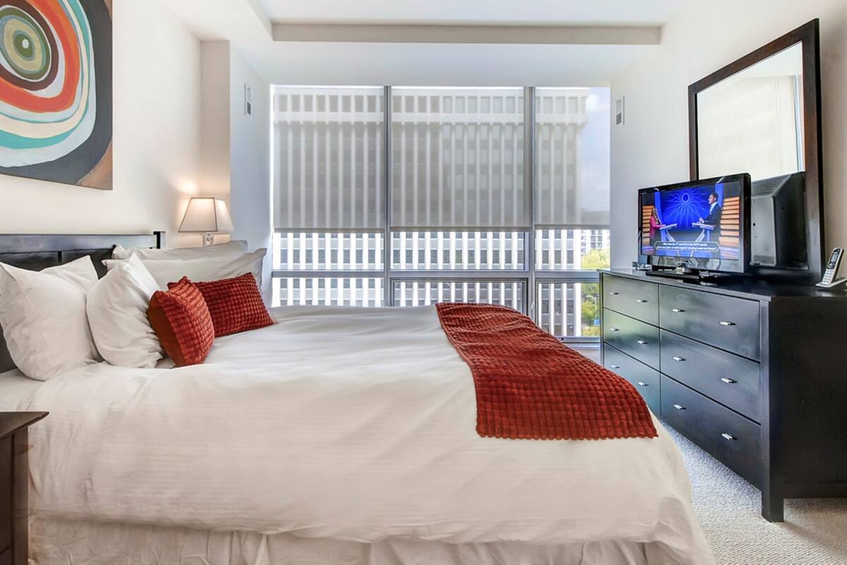 Een hotelkamer met een groot bed, een televisie, een dressoir en een raam met luxaflex.