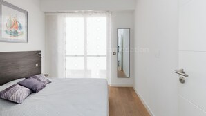 A bedroom with a bed, a nightstand, a window with curtains, and a door. - Sparkle-2189-Contemporary one-bedroom flat in the city centre (Cannes)