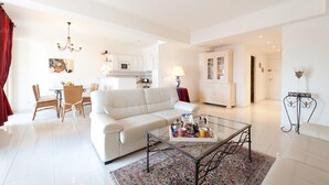 Ein modernes Wohnzimmer mit einem weißen Sofa, einem Glastisch und einem Essbereich mit Korbstühlen.