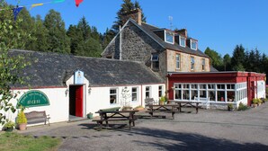 A traditional stone building with a red and white facade, a stone chimney, and a wooden bench outside. - Invershin Hotel Bunkhouse & Bar (Invershin)