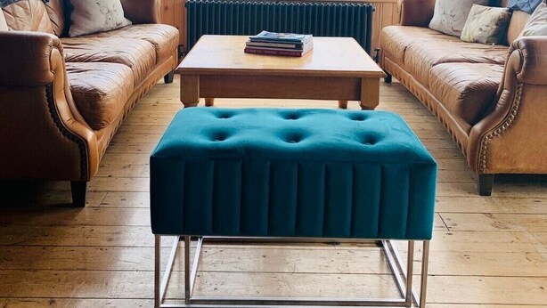 A cozy living room with a wooden floor, two brown leather sofas, a teal ottoman, and a wooden coffee table. - Invershin Hotel Bunkhouse & Bar (Invershin)