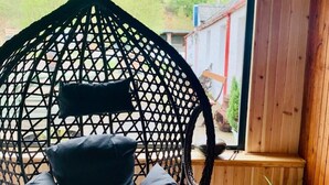 A black hanging chair with cushions in a room with wooden walls and a large window. - Invershin Hotel Bunkhouse & Bar (Invershin)