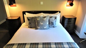 A neatly made bed with a plaid bedspread, two decorative pillows with animal prints, and two bedside tables with lamps. - Invershin Hotel Bunkhouse & Bar (Invershin)