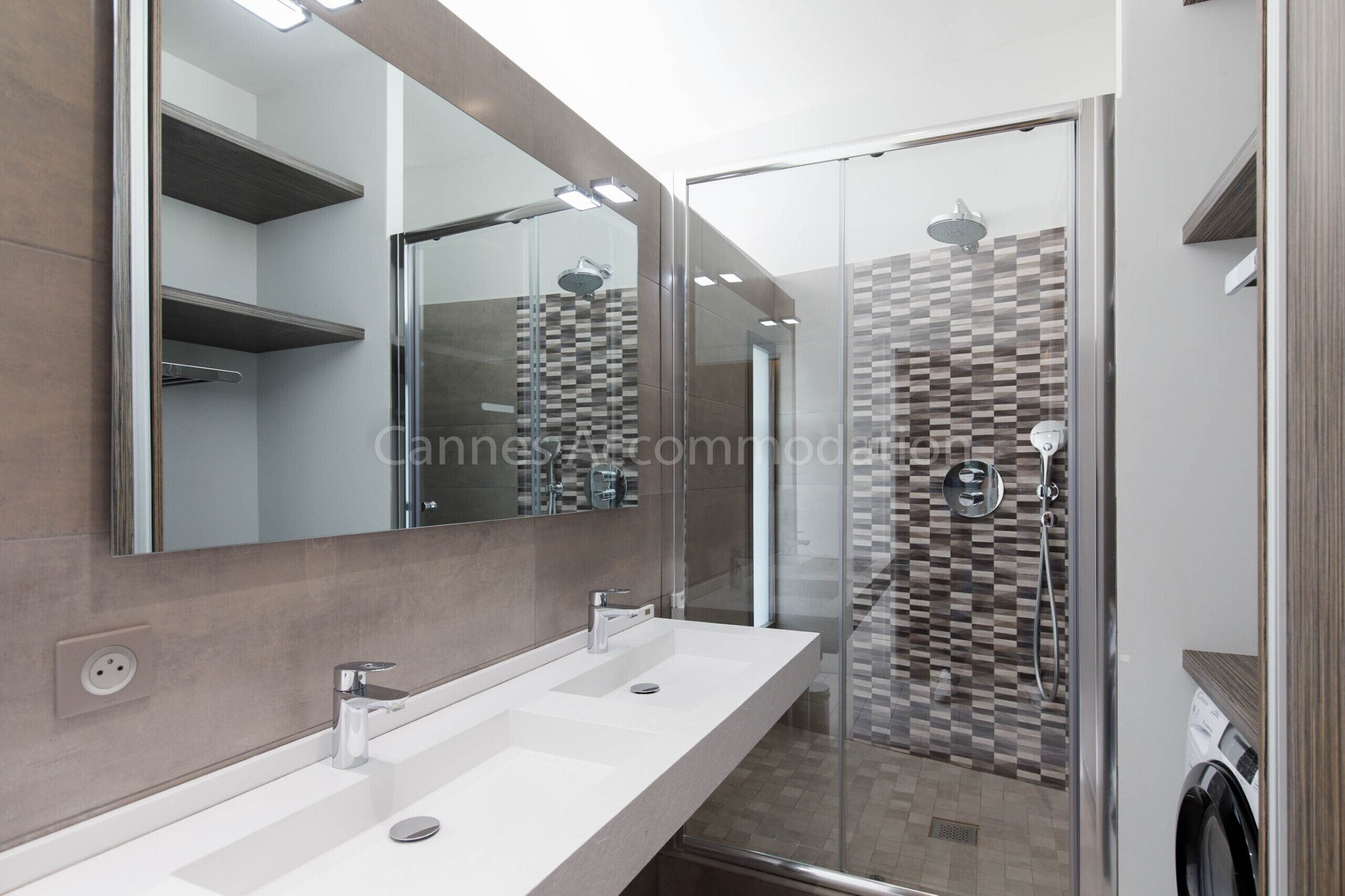 Een moderne badkamer met een grote spiegel, twee wastafels, een douche en een douchecabine met glazen wanden.
