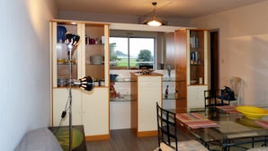 A compact kitchen with a dining area, featuring a window with a view of greenery outside, a built-in bookshelf, and a dining table with chairs. - GRAND STUDIO sea view, 47M2 tastefully decorated, 3 stars (Dinard)