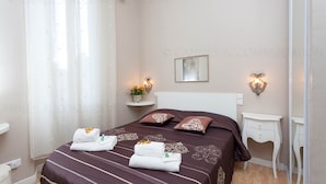 Ein ordentlich bezogenes Bett mit Handtüchern, ein Nachttisch mit Lampe und ein an der Wand hängendes Bild.