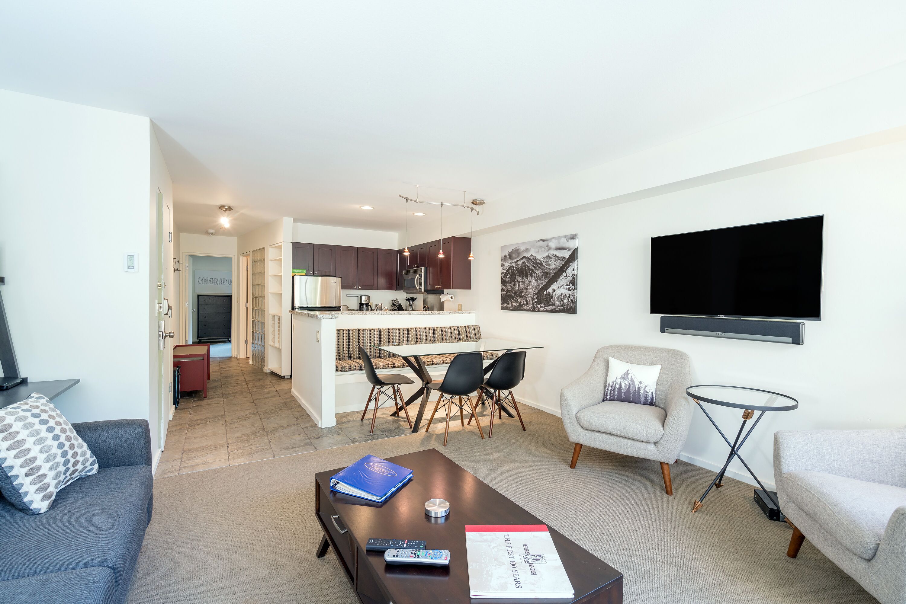 A modern living room with a sofa, a coffee table, a TV, and a dining area with chairs.