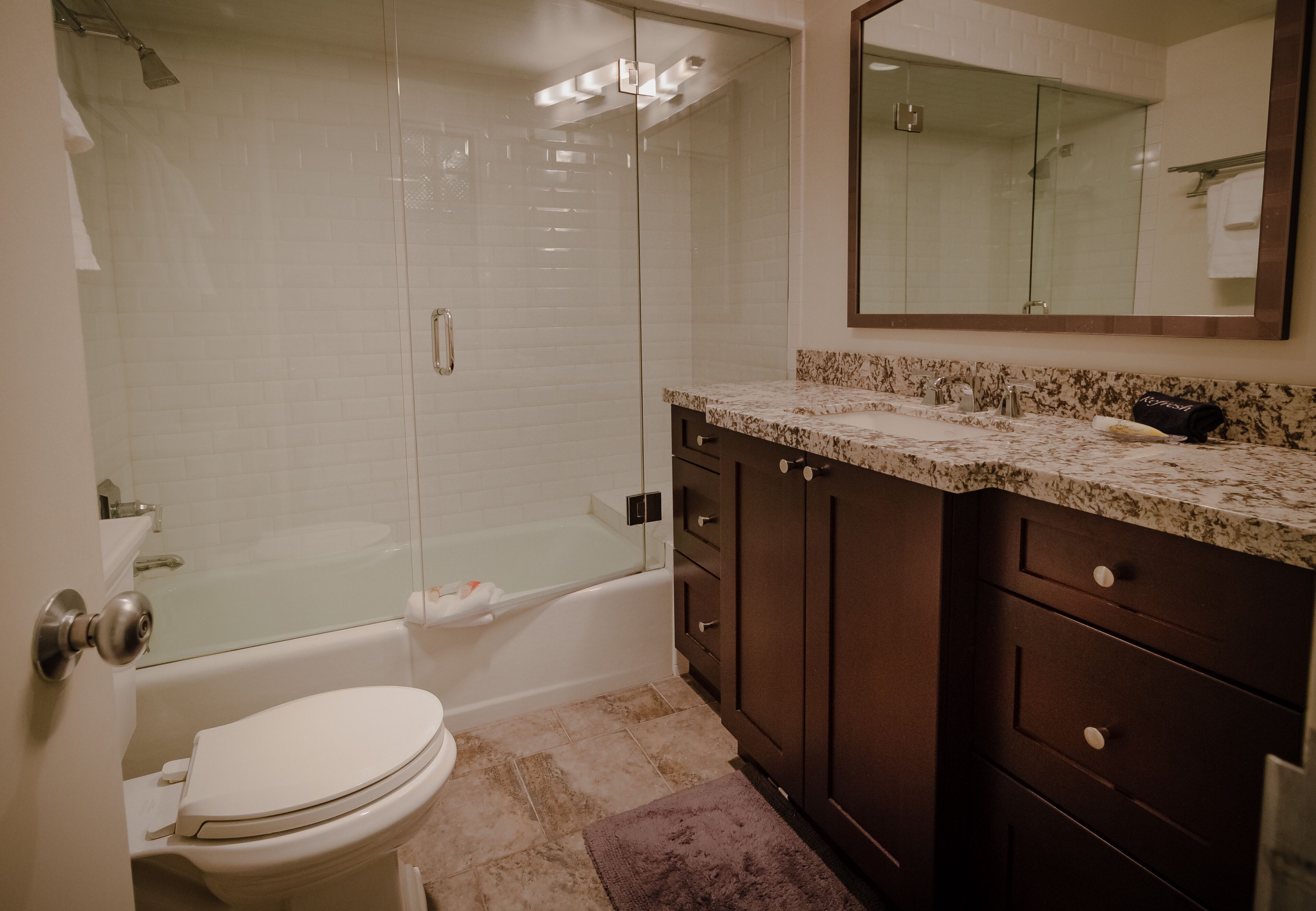 A bathroom with a glass-enclosed shower, a white toilet, a marble countertop, and dark wooden cabinets.