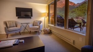 A room with two armchairs, a small table, a TV mounted on the wall, and a window with a mountain view. - Deluxe Unit with Unbeatable Deck Views (Telluride)