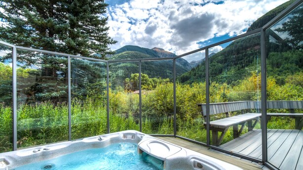 A hot tub with a mountain view, surrounded by glass walls and a wooden deck. - Deluxe Unit with Unbeatable Deck Views (Telluride)