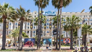 A historic building with multiple balconies, palm trees, and various movie posters advertising films like 'Mad Max Fury Road' and 'Pixels'. - Antares Pop-1694-Roomy studio in a sought-after central location. (Cannes)