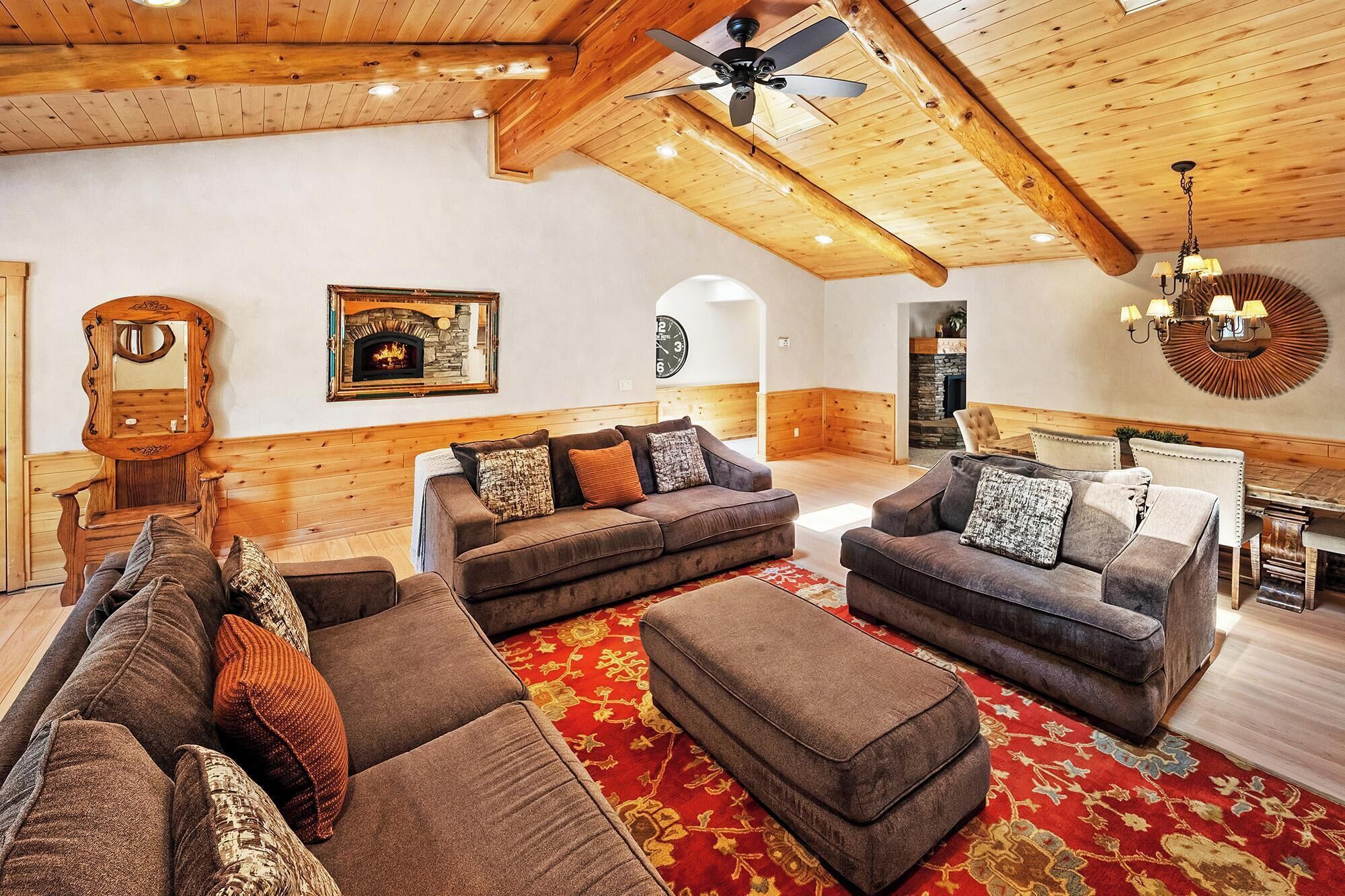 A spacious living room with a high ceiling, wooden beams, a fireplace, and a large mirror.