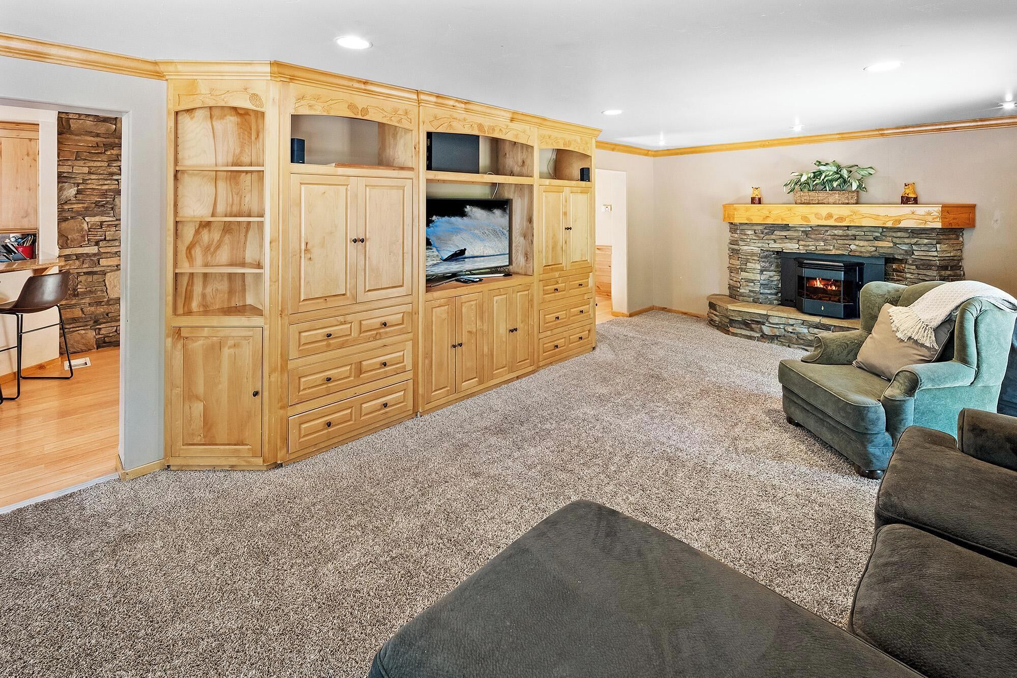 A living room with a stone fireplace, a large wooden entertainment center, and a cozy seating area.