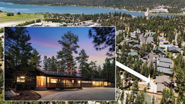 A lodge with a large driveway, surrounded by dense forest and a lake view.