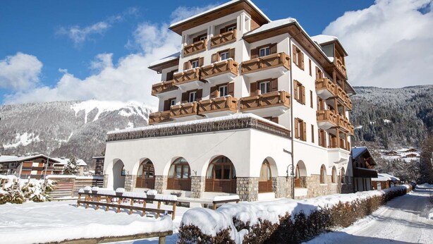 Ein mehrstöckiges Hotel mit Balkonen, Bogenfenstern und verschneiter Landschaft im Hintergrund.