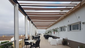 A covered outdoor terrace with tables and chairs, potted plants, and a view of the cityscape. - Hotel Almedina Spa (Medina-Sidonia)