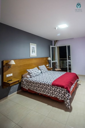 Quarto de hotel com cama, mesa de cabeceira, luminária e vista para o exterior.