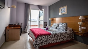 A hotel room with a bed, a desk, a chair, a nightstand, a lamp, and a window with curtains. - Hotel Almedina Spa (Medina-Sidonia)