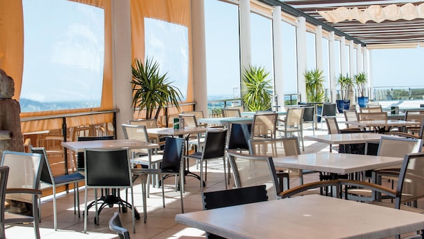 An outdoor cafe with tables and chairs, large windows, and potted plants. - Hotel Almedina Spa (Medina-Sidonia)
