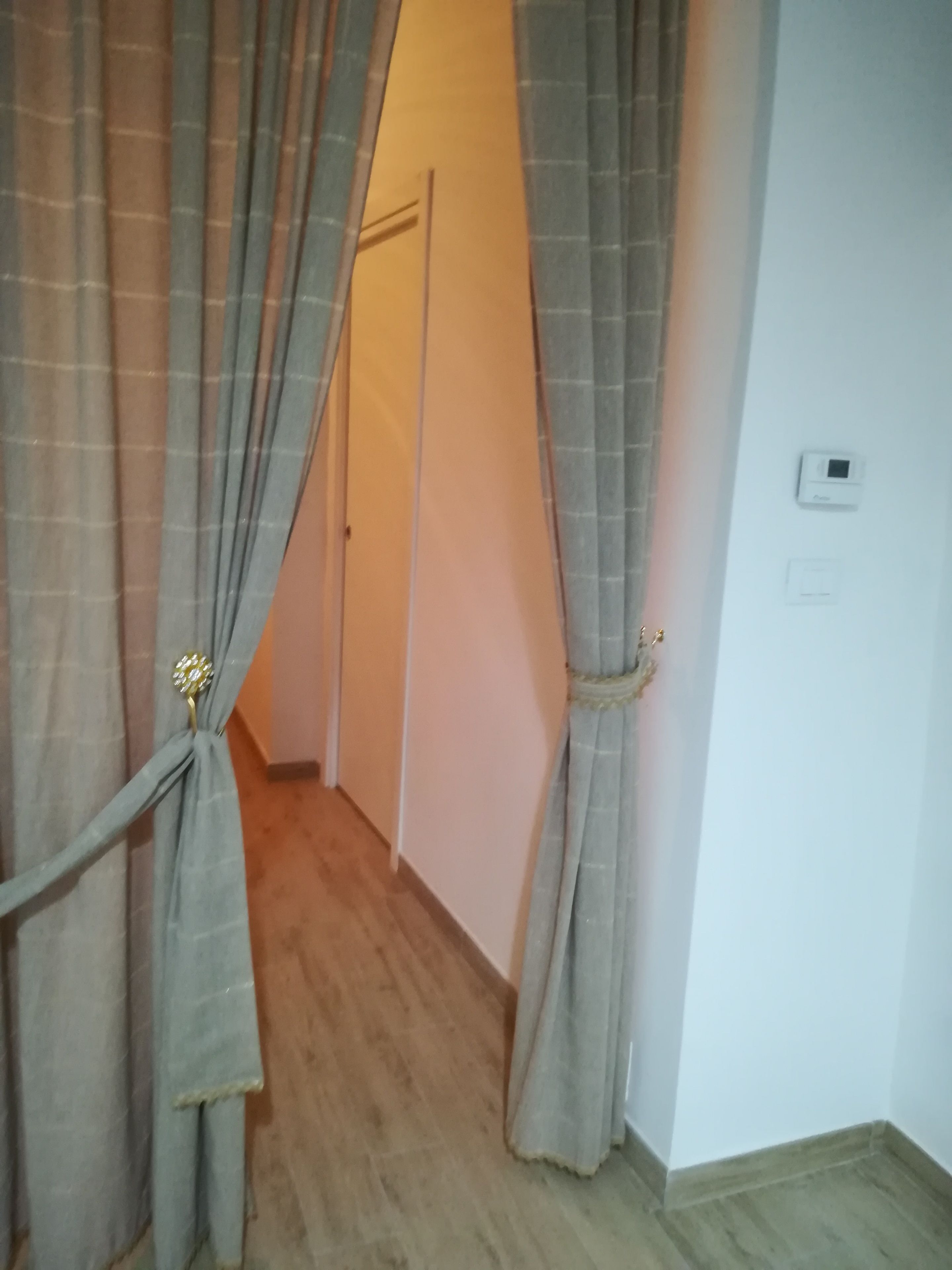 Ein Flur mit Holzboden, einer Tür am Ende und einem Thermostat an der Wand.