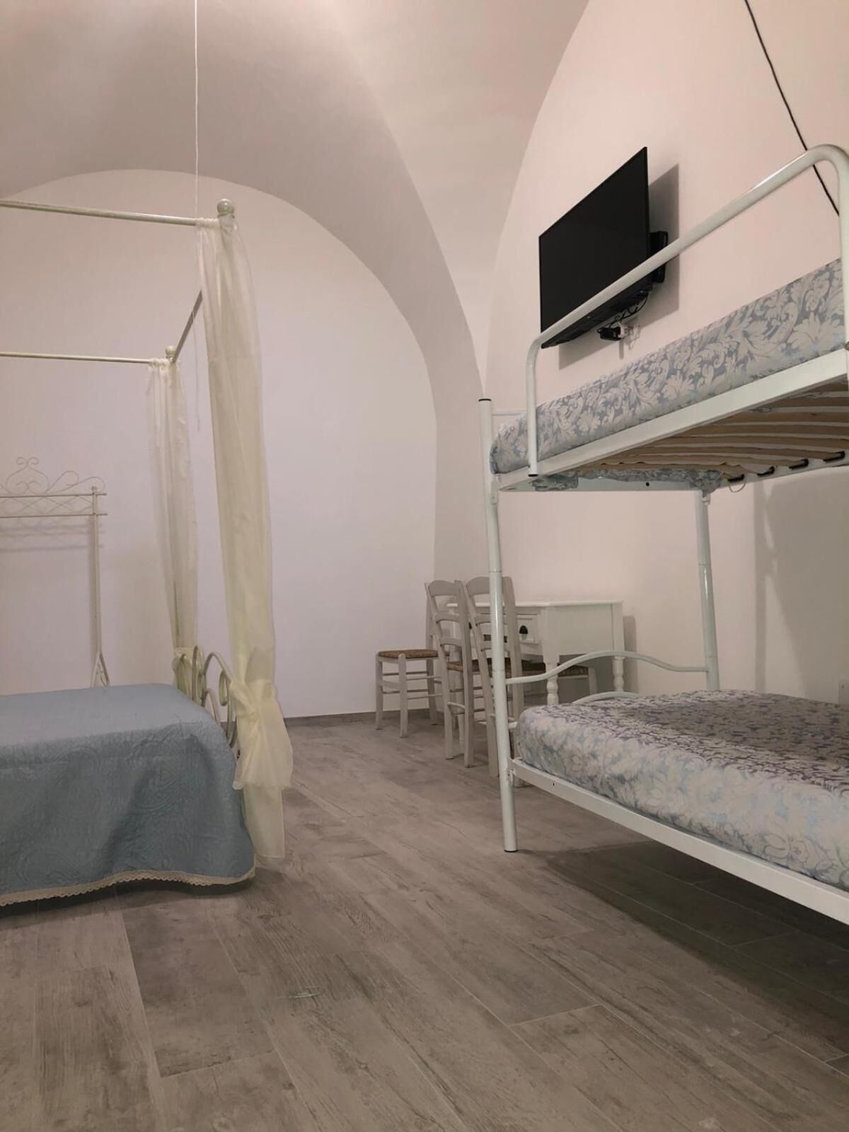 A dormitory room with bunk beds, a desk, a chair, and a TV mounted on the wall.