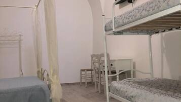 A dormitory room with bunk beds, a desk, a chair, and a TV mounted on the wall.