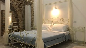 Una cama con estructura metálica y dosel blanco, una pared de piedra y un espejo a la izquierda.