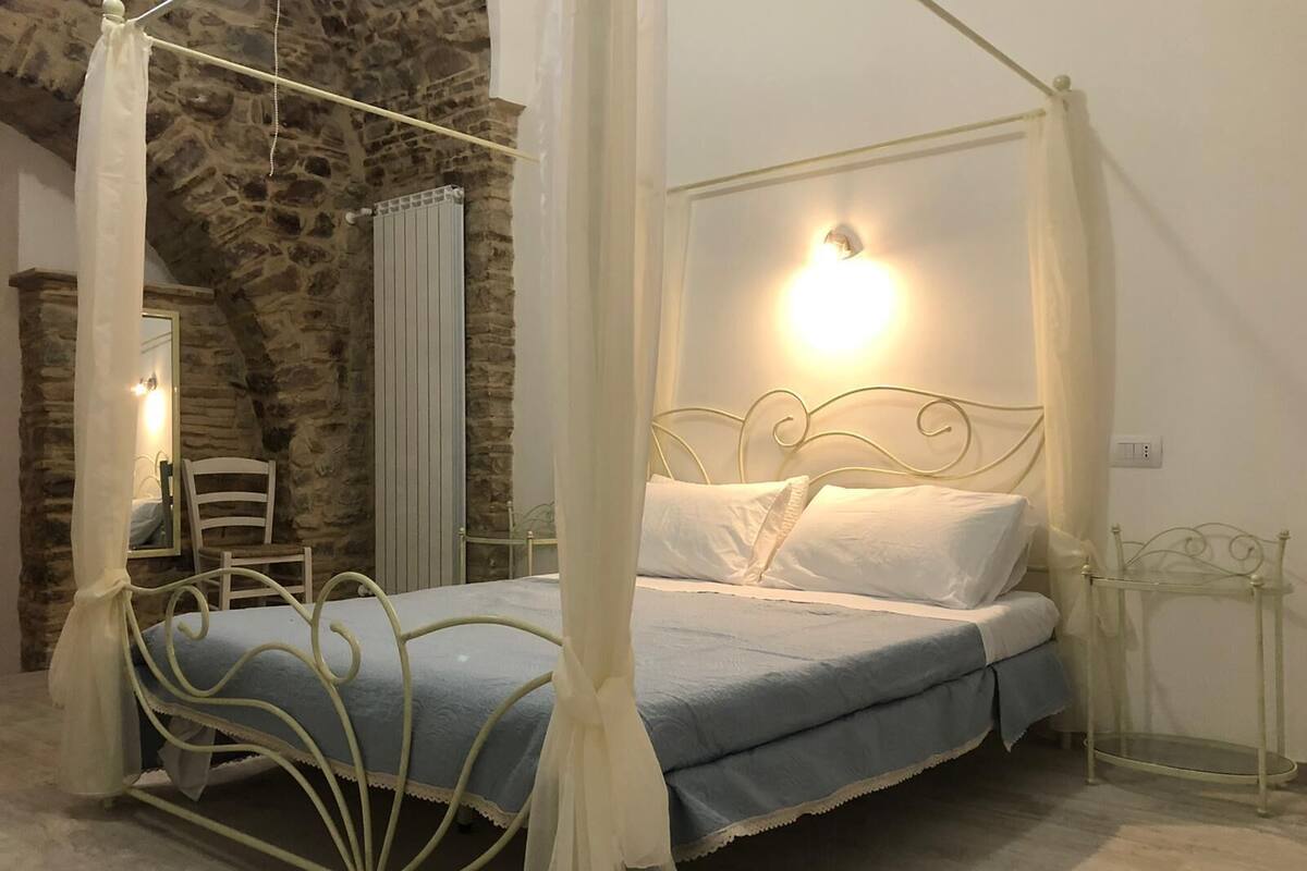A bed with a metal frame and white canopy, a stone wall, and a mirror on the left.