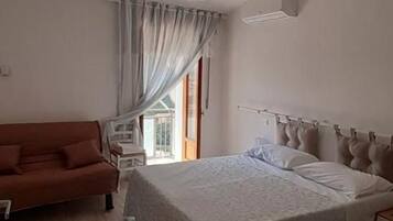 A bedroom with a bed, a sofa, a desk, and a window with curtains.