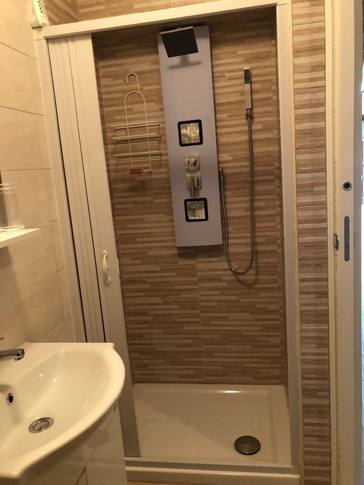 A shower with a control panel, a handheld showerhead, and a wall-mounted towel rack.