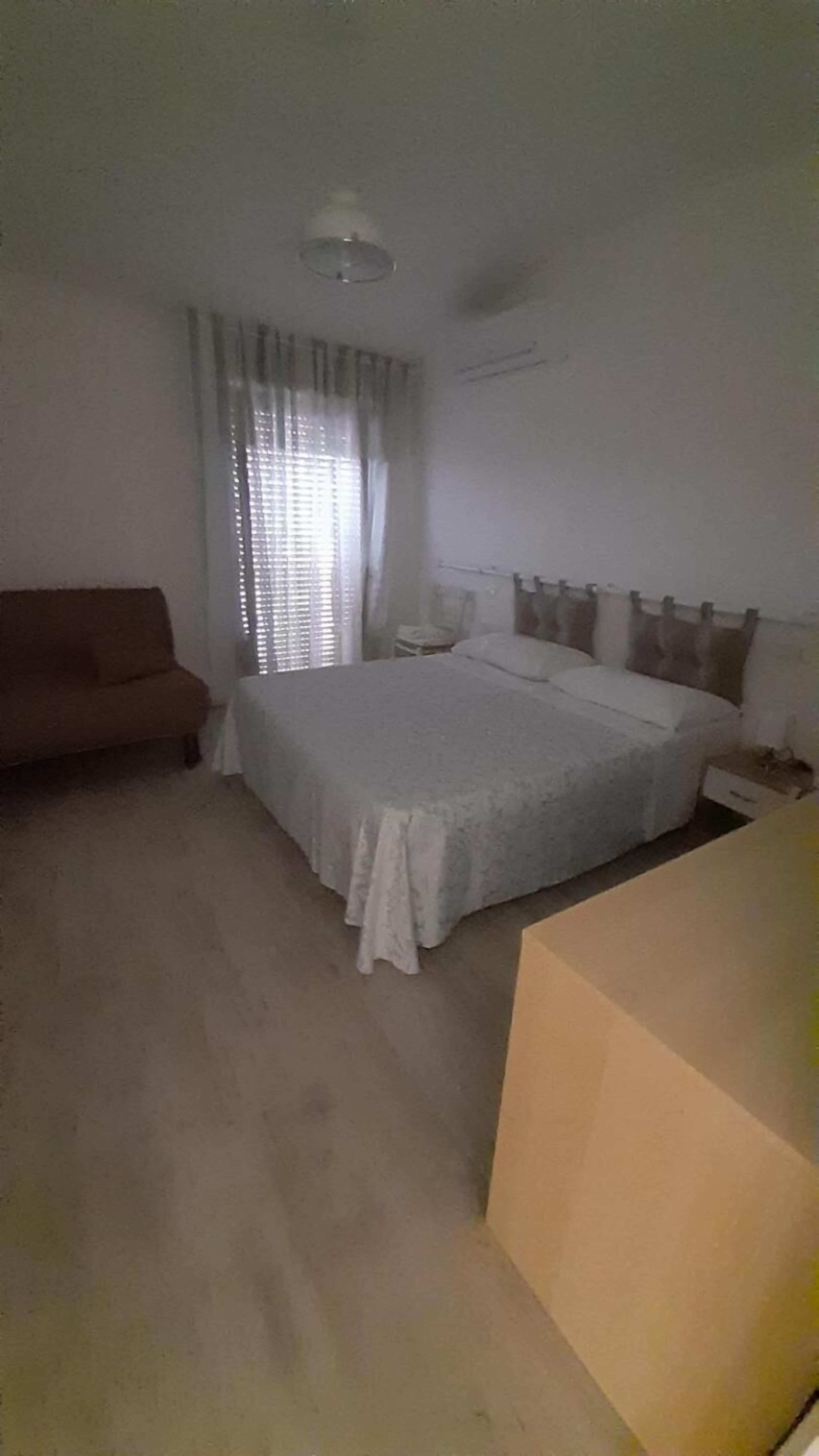 A bedroom with a bed, a nightstand, a sofa, and a large cardboard box.
