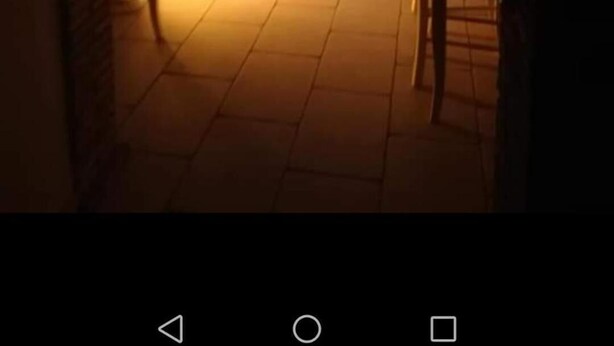 Un comedor con mesas y sillas de madera, una pared de piedra y suelo de baldosas.