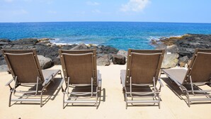 Four lounge chairs facing the ocean with a rocky shoreline and clear blue sky. - LAST MINUTE DISCOUNT SPECIALS! End Unit. Direct Ocean View. Wrap-Around Lanai. (Kailua-Kona)