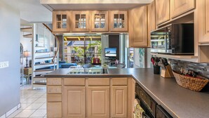A kitchen with wooden cabinets, a central island, a microwave, and a large window. - LAST MINUTE DISCOUNT SPECIALS! End Unit. Direct Ocean View. Wrap-Around Lanai. (Kailua-Kona)