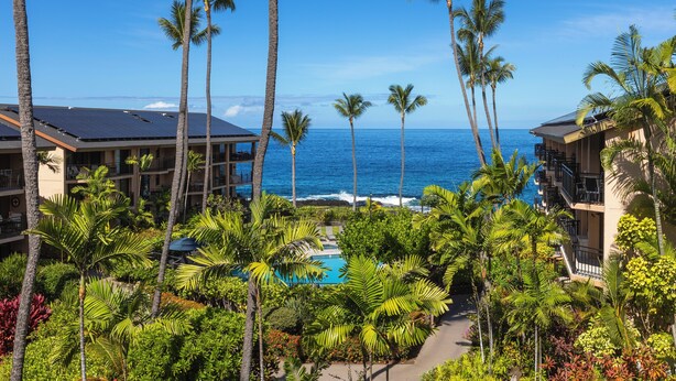 A resort with a pool surrounded by palm trees and a view of the ocean. - LAST MINUTE DISCOUNT SPECIALS! End Unit. Direct Ocean View. Wrap-Around Lanai. (Kailua-Kona)