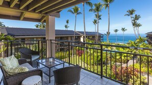 A balcony with wicker furniture, a glass table, and a view of the ocean and palm trees. - LAST MINUTE DISCOUNT SPECIALS! End Unit. Direct Ocean View. Wrap-Around Lanai. (Kailua-Kona)