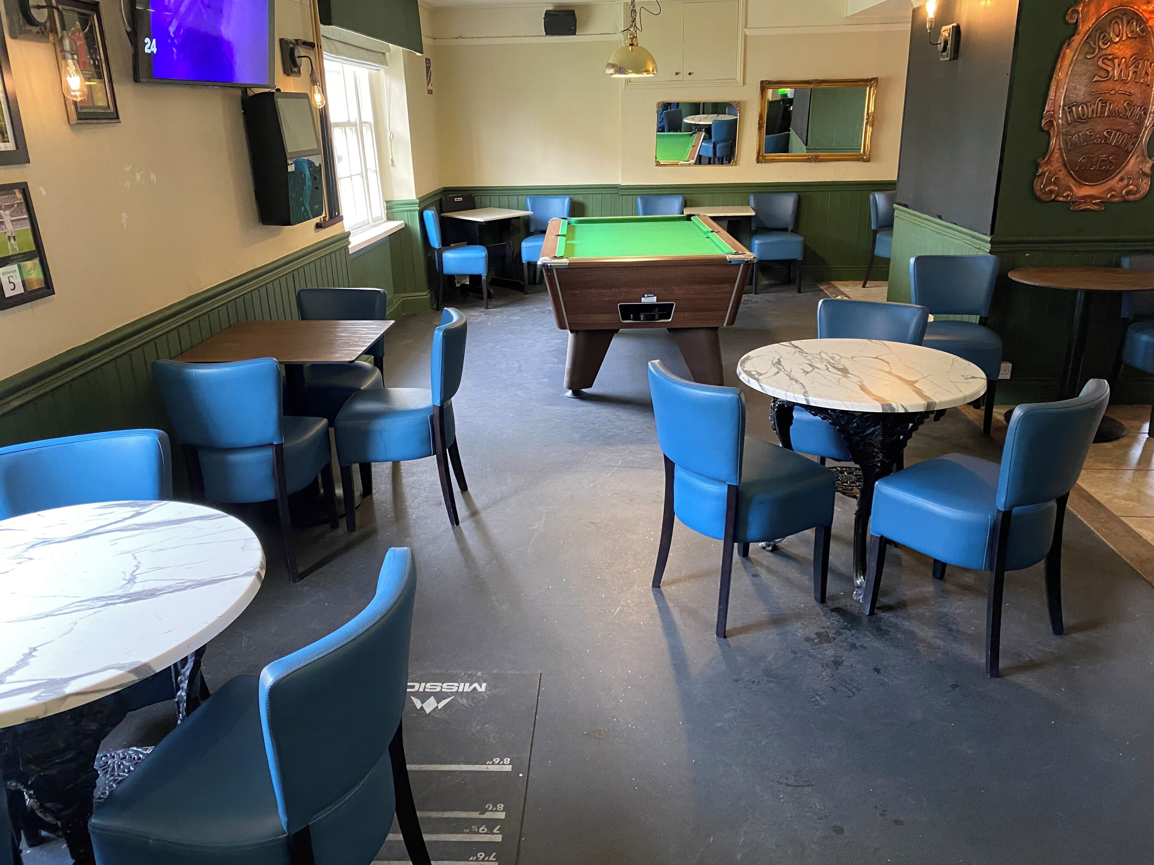 A billiards room with tables and chairs, a pool table, and a television screen.