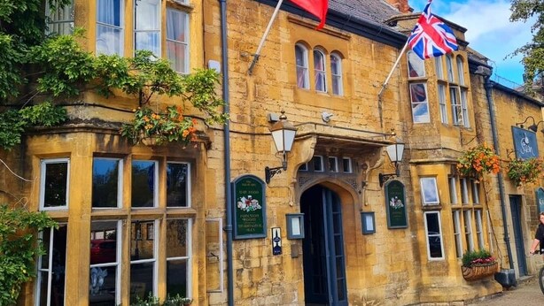 A historic stone building with arched windows and a flagpole. - The Swan Inn (Moreton-in-Marsh)